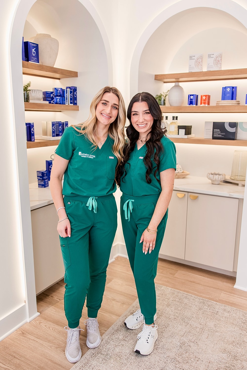 Two women in matching green uniforms smiling together.