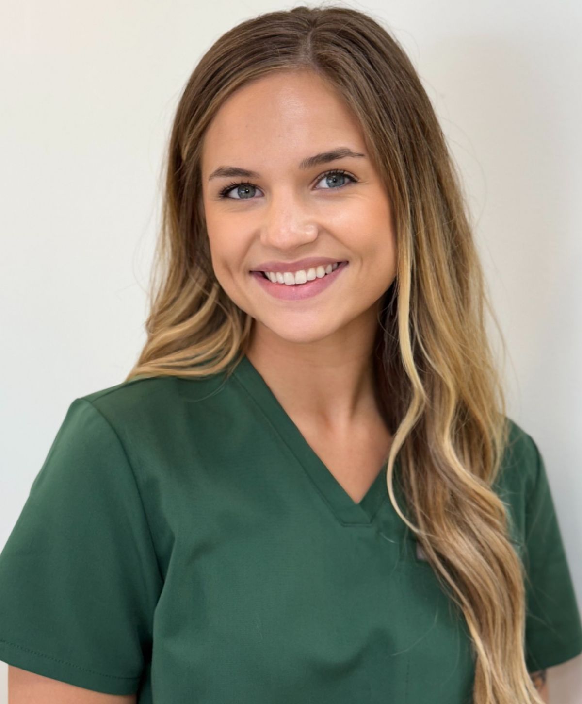 Smiling woman in green scrubs against white background.