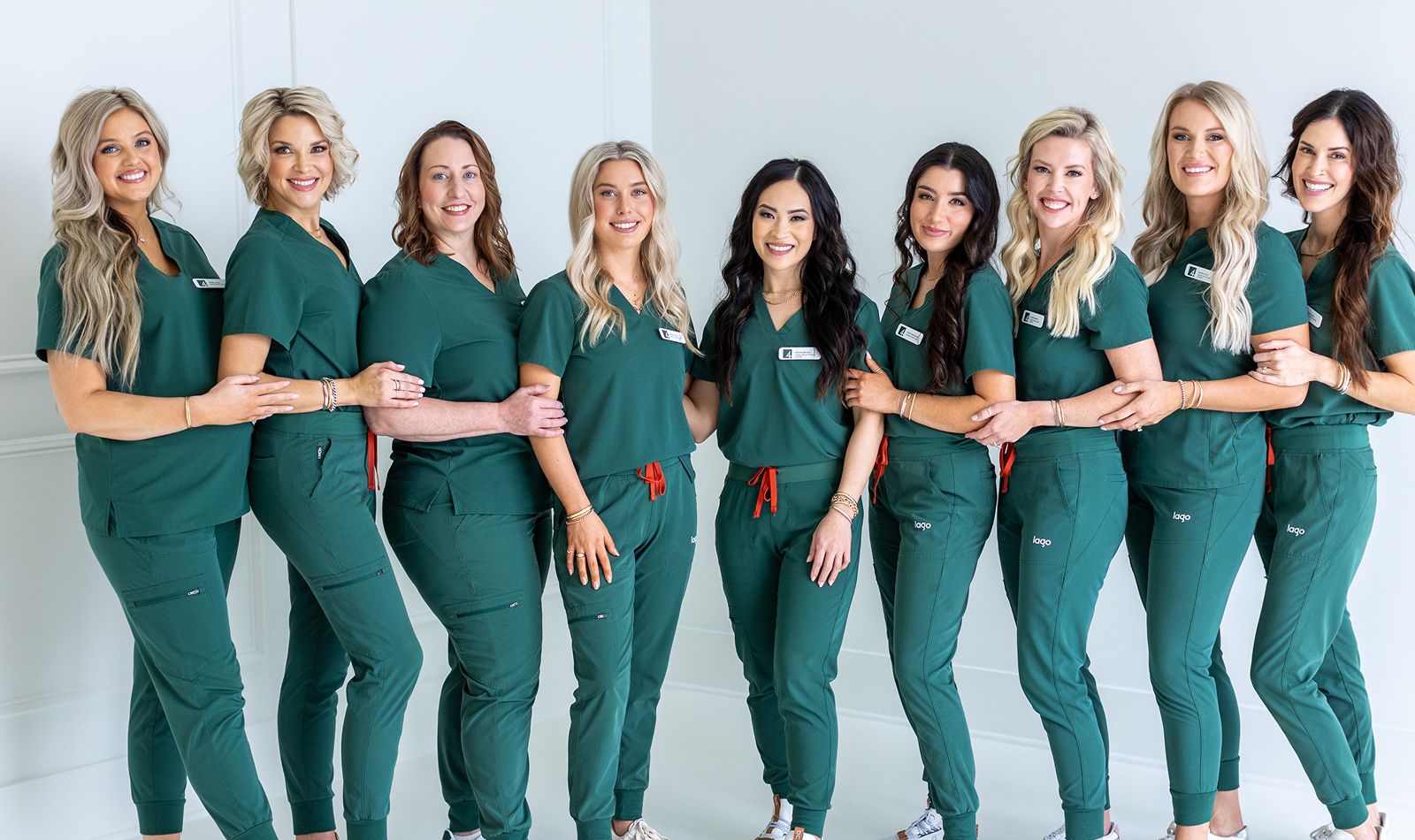 Group of women in green scrubs smiling together.